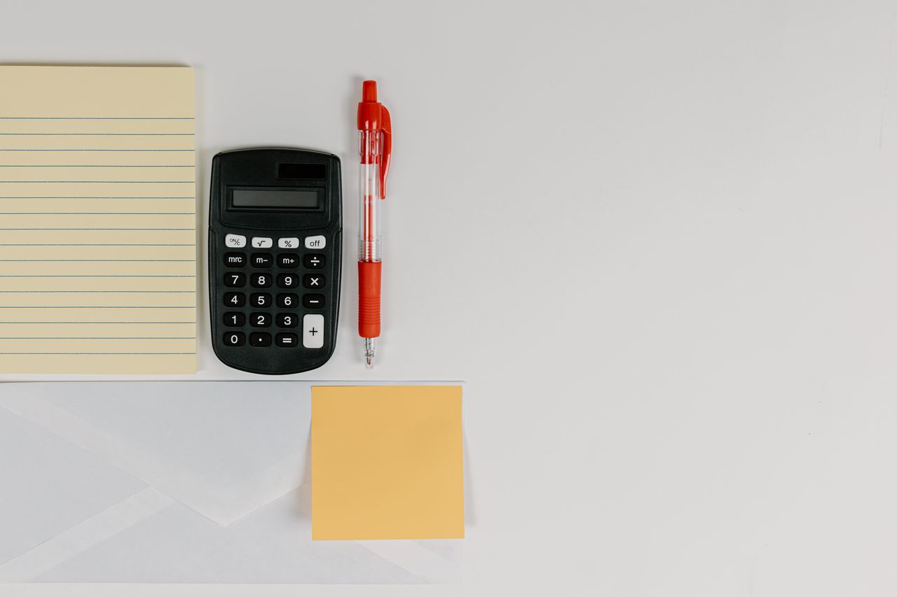 Top view of calculator, pen, and note pads arranged neatly on a white surface.